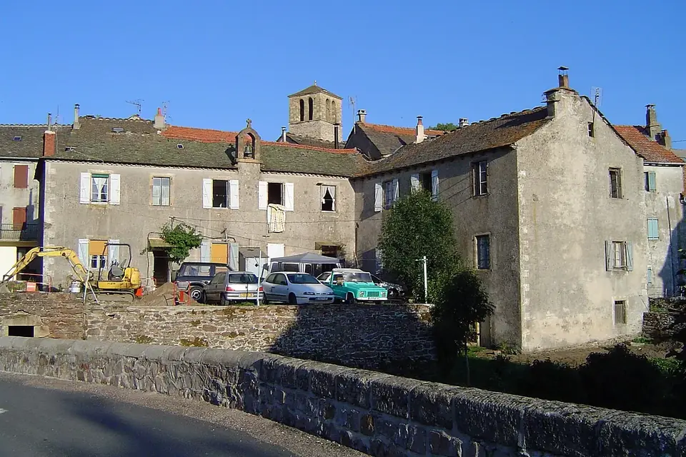 Maisons de pierre d'un village de Lozère au bord d'une rivière, avec l'église et son clocher à l'arrière-plan
