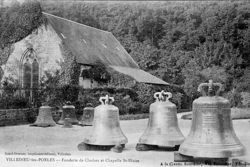 Ancienne carte postale montrant plusieurs grosses cloches neuves alignées devant une chapelle, à la sortie d'une fonderie