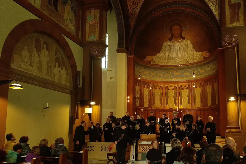 Chœur et orchestre en concert dans le chœur d'une église abbatiale peinte, devant un public assis dans la nef