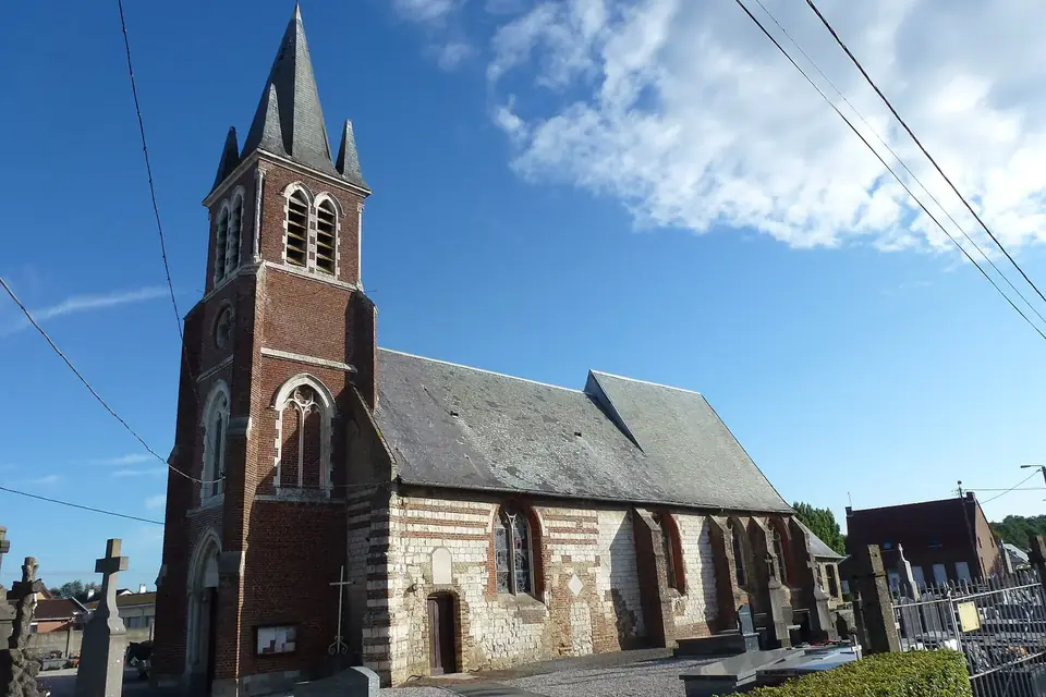 Église de village en brique et pierre avec un haut clocher pointu, sous un ciel bleu