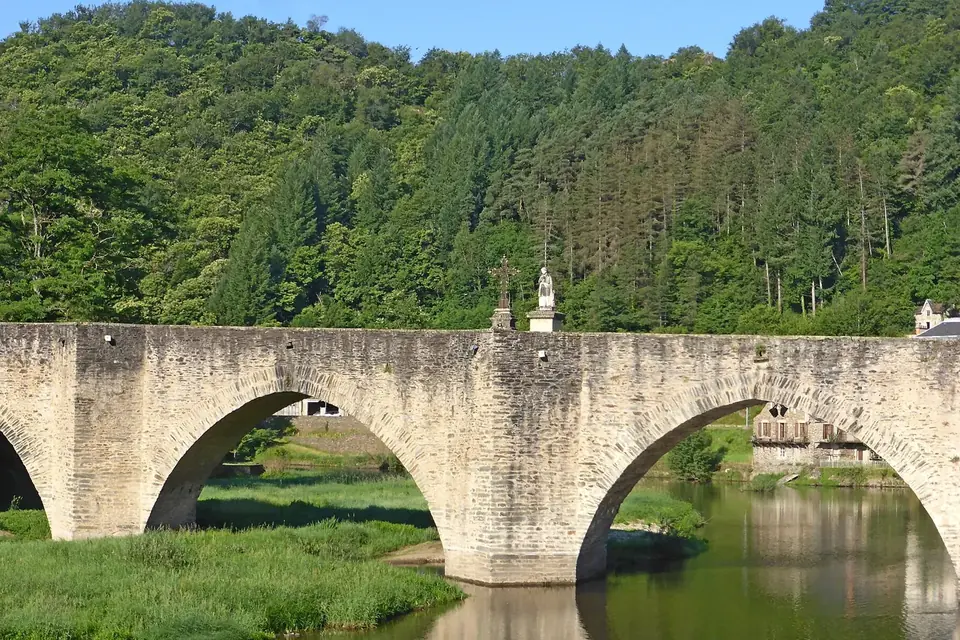 Pont gothique de pierre à plusieurs arches franchissant le Lot à Estaing, devant une colline boisée