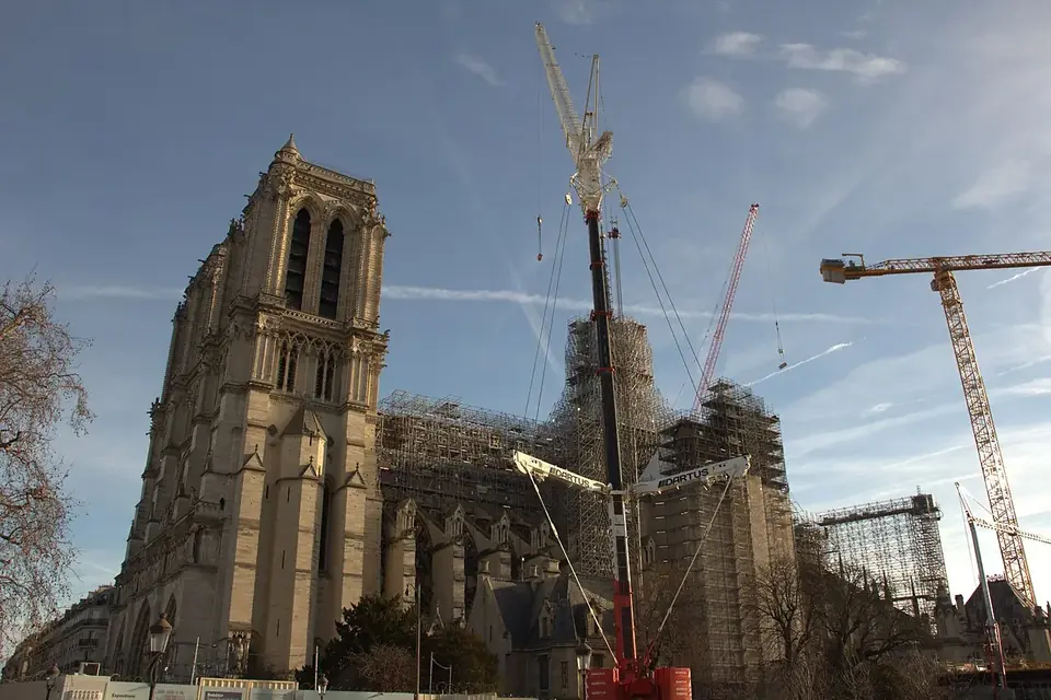 Façade et flanc de Notre-Dame de Paris entourés d'échafaudages et de grues, sous un ciel bleu