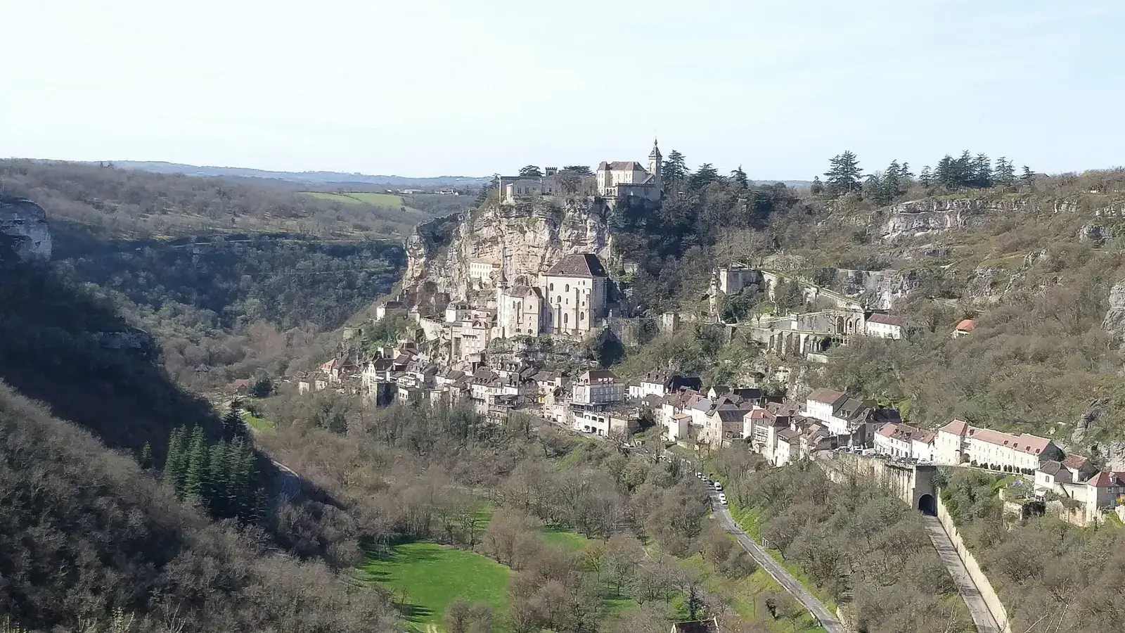 Le village de Rocamadour accroché à une falaise au-dessus d'une vallée boisée, dans la lumière du matin